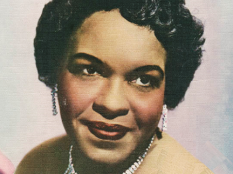 A coloured photograph of pianist Winifred Atwell wearing silver earrings and a necklace.